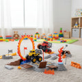 Toy monster truck set with obstacles on a carpeted floor in a room with toys in the background