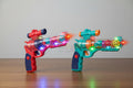 Two colorful toy guns with LED lights on a wooden surface.