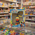 A boxed Mickey Mouse Clubhouse toy helicopter displayed on a glass shelf in a toy store. The package shows a yellow helicopter with an orange beak and blue outfit, with Mickey Mouse and Donald Duck printed on the front.