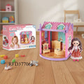 Dollhouse with furniture and a doll, next to its packaging on a wooden floor.