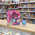 A boxed toy hovering helicopter with a matching blue unicorn ball and a small black hovering helicopter displayed on a wooden counter in a toy store. The retail box is pink and blue with unicorn graphics and the text 'Scout's Caballo' and 'EASY TO USE!'.