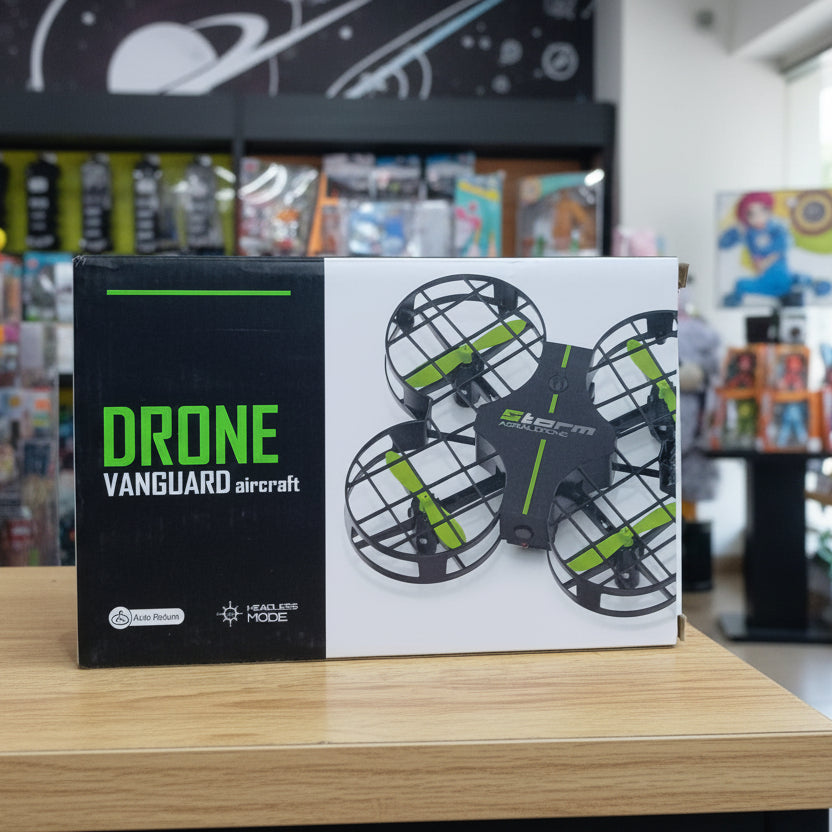 A boxed drone product labeled 'DRONE VANGUARD aircraft' standing on a wooden table in a retail store. The box is black and white with bright green text and shows a black quadcopter drone with green accents on the front.