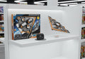 A toy spaceship model and its controller displayed on a white retail shelf next to the product packaging box, with toy shelves and other items blurred in the background.