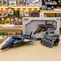 A toy combat dart gun flying craft set displayed on a wooden table in a toy store, featuring a blue and black dart gun, a gray multi-pronged dart gun, and its original product packaging box in the background.