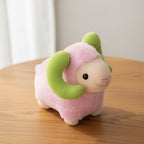 Pink plush toy with green horns on a wooden surface