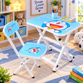A children's folding desk and chair set with a bright blue Doraemon-themed print, shown in a styled room setting with a bookshelf, rug, and toys.