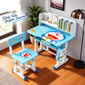 A children's desk and chair set in a bright room, featuring a light blue and white design with Doraemon graphics. The set includes a height-adjustable desk with a built-in bookshelf, a matching chair, and a side storage bag.